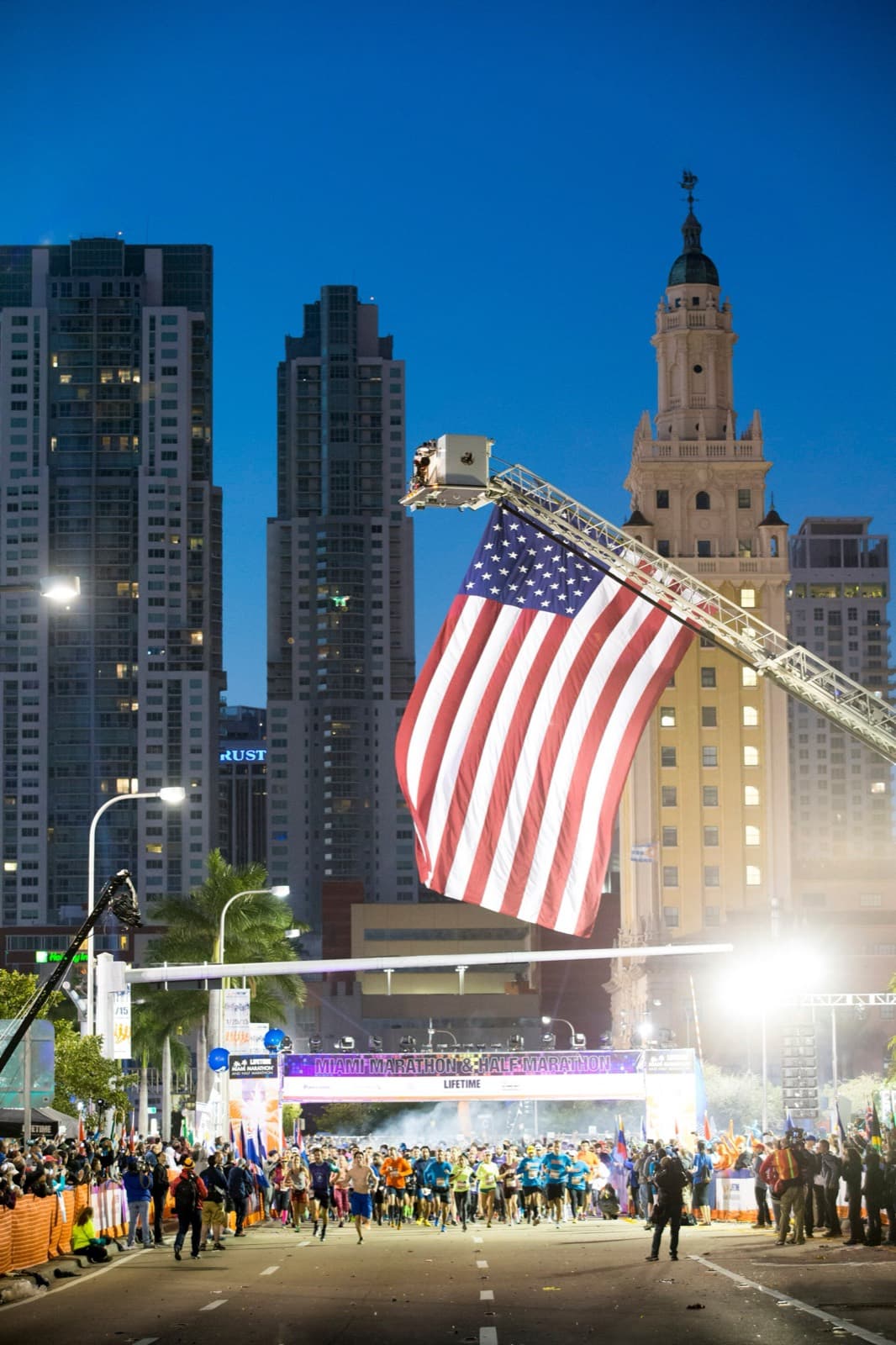 Life Time Miami Marathon: runners leaving the start line on biscayne blvd under a large flag before dawn