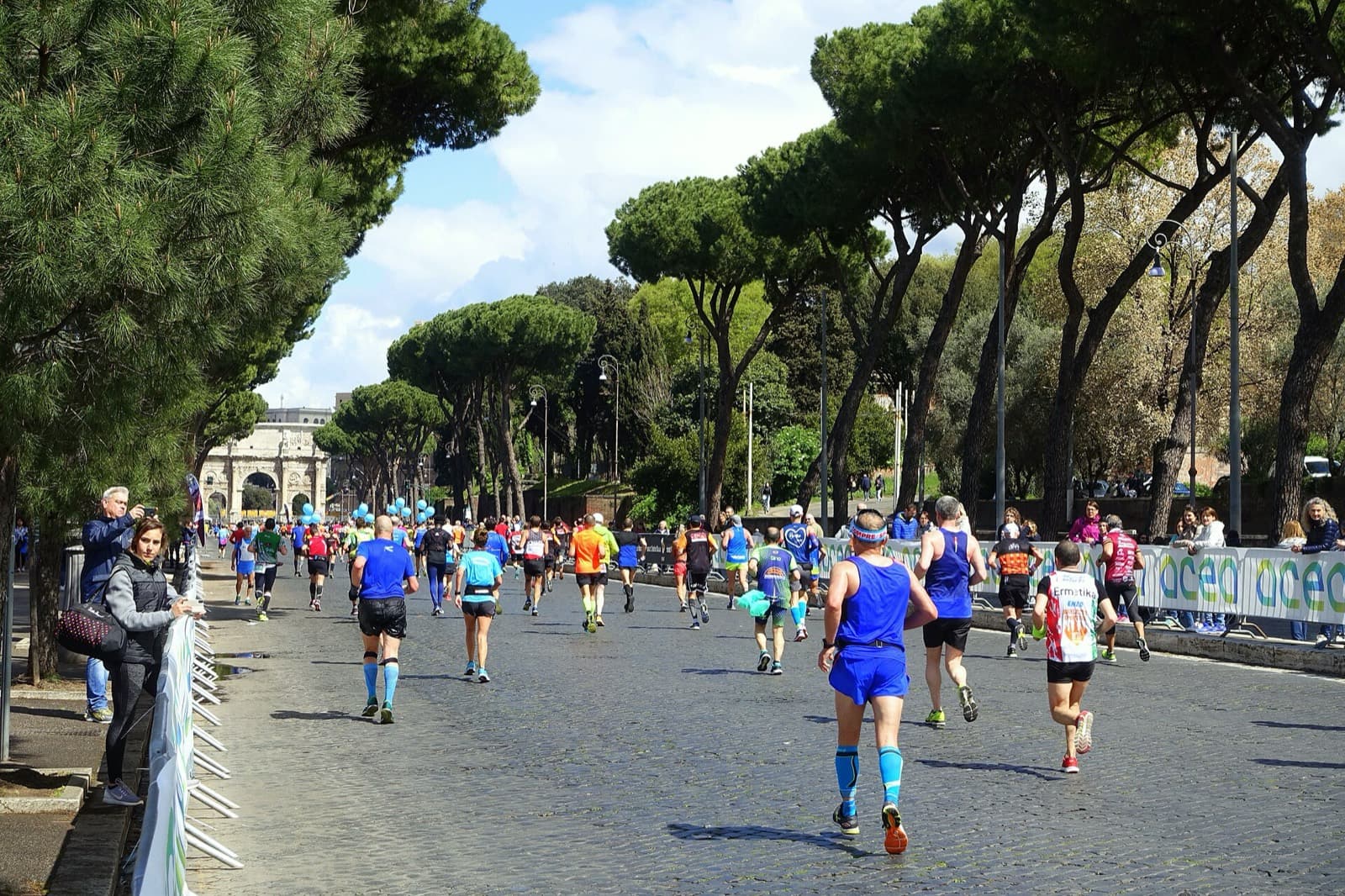 Acea Run Rome The Marathon: runners under umbrella pines on via di san gregorio, arch of constantine behind