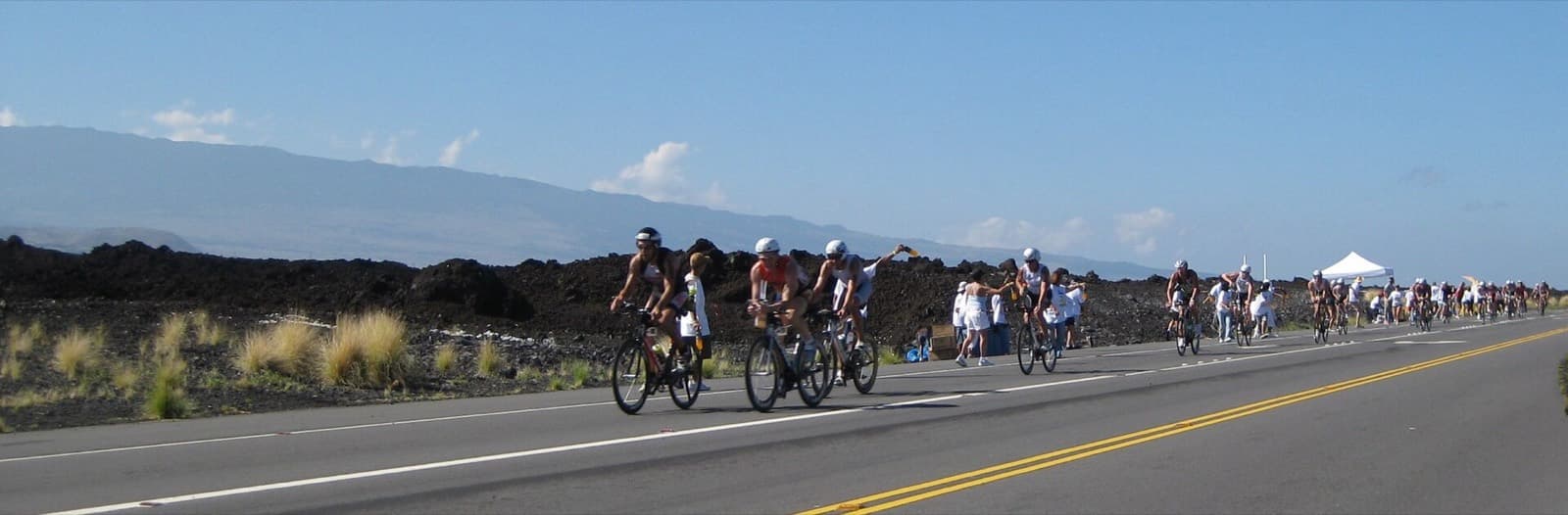 IRONMAN 70.3 Hawai`i (Honu): cyclists on the queen k highway past lava fields at the mauna lani aid station